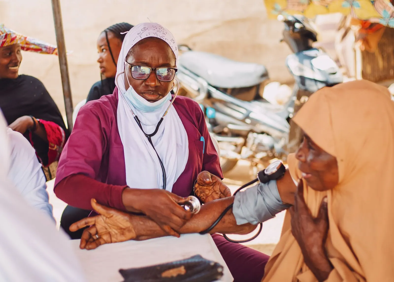 Health worker in a white hijab checking the blood pressure of a woman in a headscarf